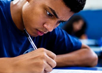 Estudante escreve redação à mão em sala de aula, com foco e concentração.