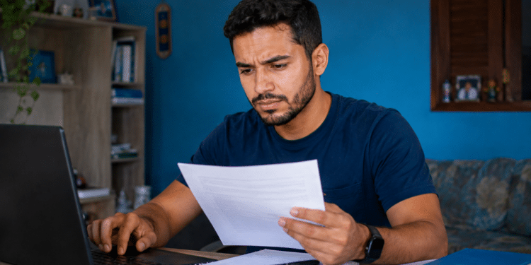 Imagem ilustrativa de candidato comparando um documento impresso com a tela do notebook, com expressão de desconfiança, cena ligada à checagem de anúncios de concurso público.