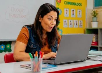 Professora da educação básica utilizando notebook em sala de aula, representando uma formação sobre inteligência artificial e educação digital.