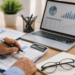 Mãos masculinas usando calculadora cercadas por gráficos, laptop com dashboard de finanças e óculos sobre caderno