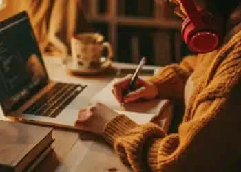 Estudante com fones de ouvido fazendo anotações durante uma graduação EAD pelo notebook.