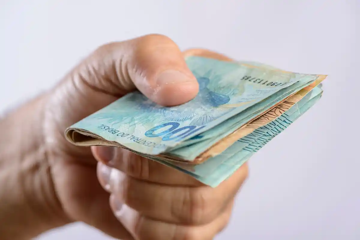 Mão segurando notas de real representando os pagamentos do INSS entre 31 de agosto e 4 de setembro.