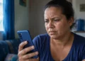 Mulher preocupada segura celular em casa durante instabilidade no acesso ao aplicativo Caixa Tem.