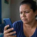 Mulher preocupada segura celular em casa durante instabilidade no acesso ao aplicativo Caixa Tem.
