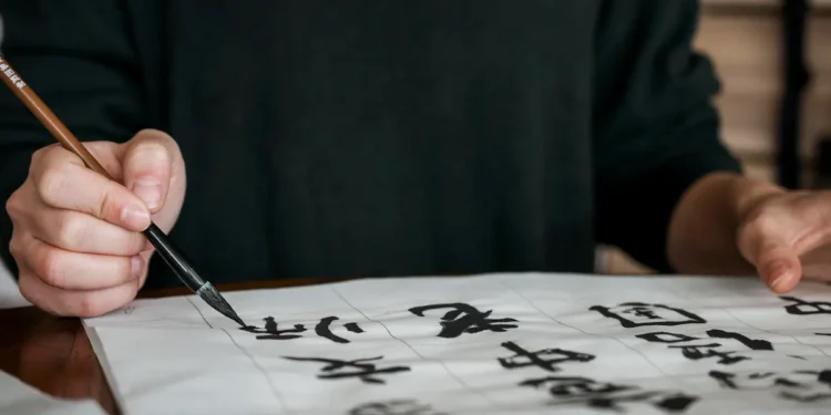 Pessoa praticando a escrita japonesa com pincel e tinta sobre papel, representando o aprendizado do idioma japonês e seus benefícios profissionais.
