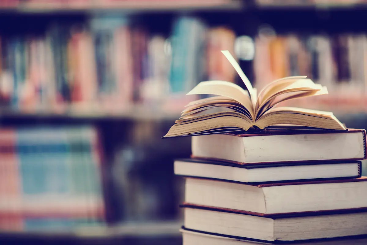 Livro aberto sobre uma pilha de livros em biblioteca, representando o universo da poesia e da literatura.