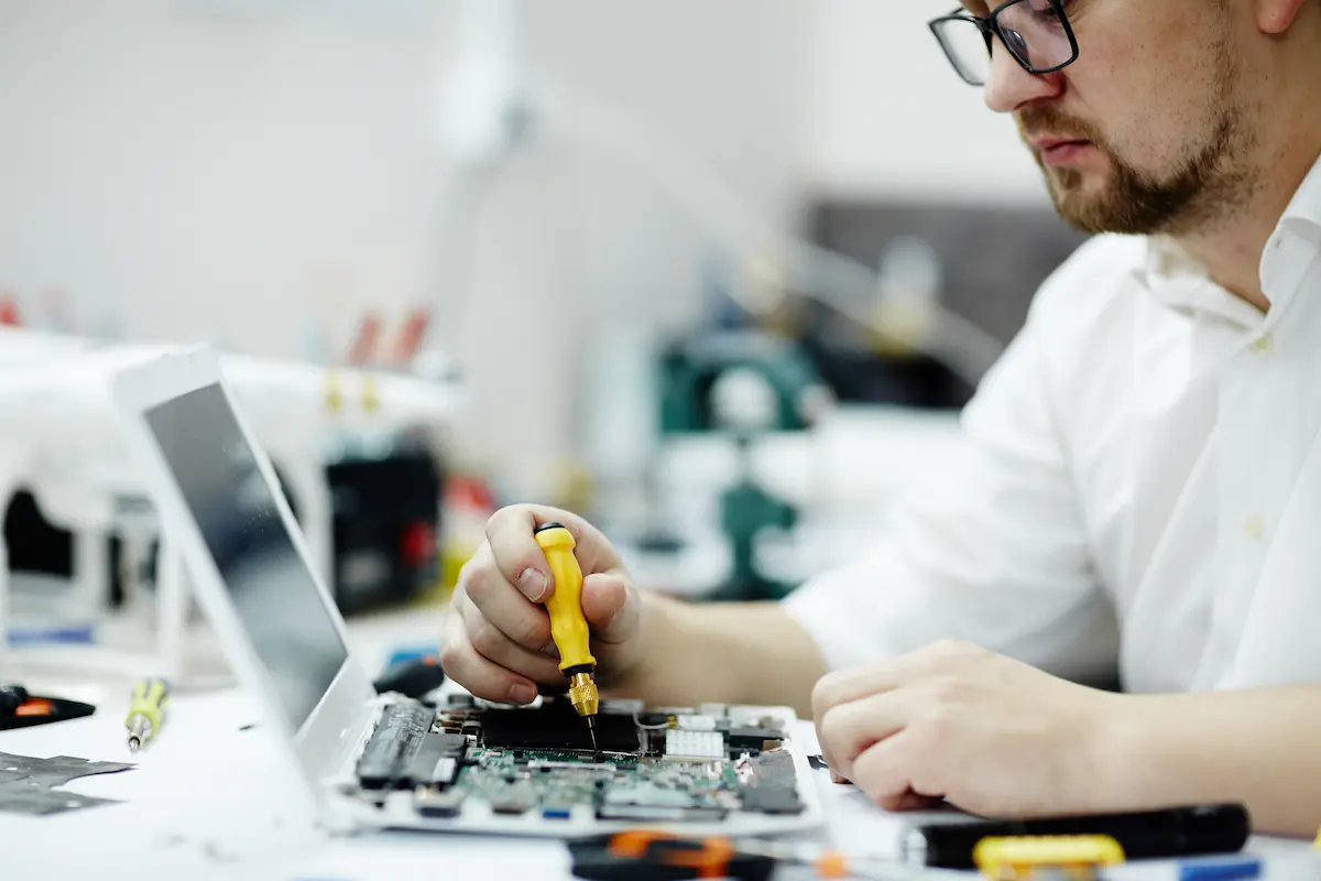 Técnico realizando manutenção em notebook durante reparo de componentes internos.