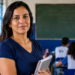 Professora posando com cadernos nos braços diante de uma turma em sala de aula de escola pública, em referência às vagas de mestrado presencial abertas pelo MEC e pela Capes