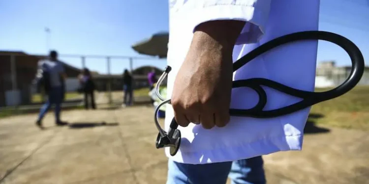 Médico segura estetoscópio em área externa representando atuação profissional em regiões com falta de médicos.