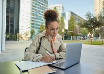 Estudante faz anotações enquanto utiliza um notebook em ambiente universitário.
