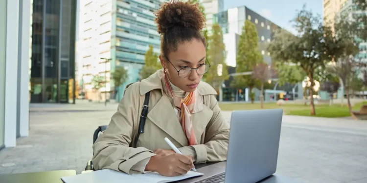 Estudante faz anotações enquanto utiliza um notebook em ambiente universitário.