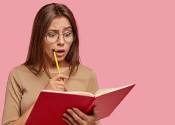 Imagem ilustrativa de mulher de óculos com expressão de espanto segurando um livro vermelho e um lápis, representando a dúvida diante de uma palavra difícil