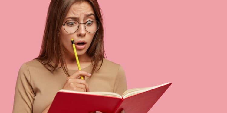 Imagem ilustrativa de mulher de óculos com expressão de espanto segurando um livro vermelho e um lápis, representando a dúvida diante de uma palavra difícil
