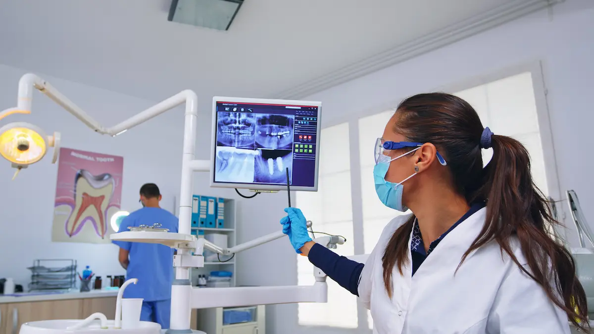 Dentista analisa radiografias odontológicas em monitor durante atendimento em consultório.