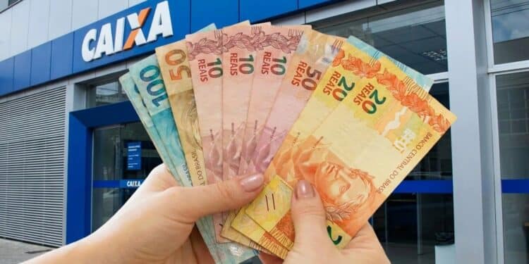 Imagem ilustrativa de mãos segurando cédulas de real em leque diante de uma agência da Caixa, representando o retorno dos pagamentos do Pé-de-Meia