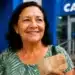 Beneficiária do INSS segura dinheiro em frente a uma agência bancária, representando os pagamentos acima do salário mínimo.