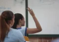 Estudante em sala de aula levanta a mão durante atividade escolar.
