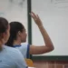 Estudante em sala de aula levanta a mão durante atividade escolar.