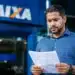 Homem segura documento em frente a uma agência da Caixa, representando o saldo do FGTS retido após pedido de demissão.