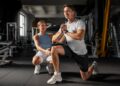 Imagem ilustrativa de personal trainer acompanhando a execução de um exercício de agachamento por um aluno dentro da academia, em referência à formação exigida para atuar na profissão