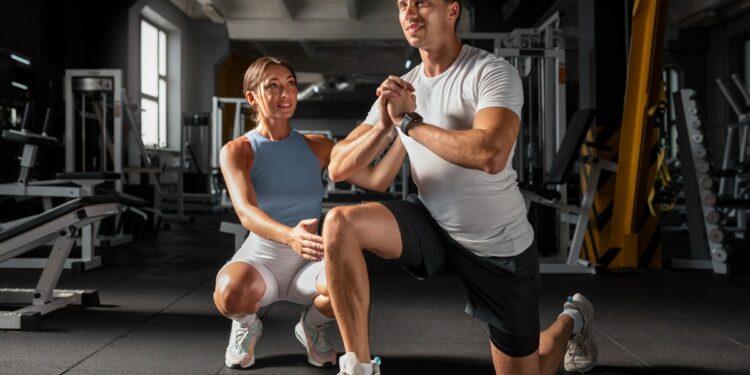 Imagem ilustrativa de personal trainer acompanhando a execução de um exercício de agachamento por um aluno dentro da academia, em referência à formação exigida para atuar na profissão