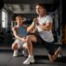 Imagem ilustrativa de personal trainer acompanhando a execução de um exercício de agachamento por um aluno dentro da academia, em referência à formação exigida para atuar na profissão