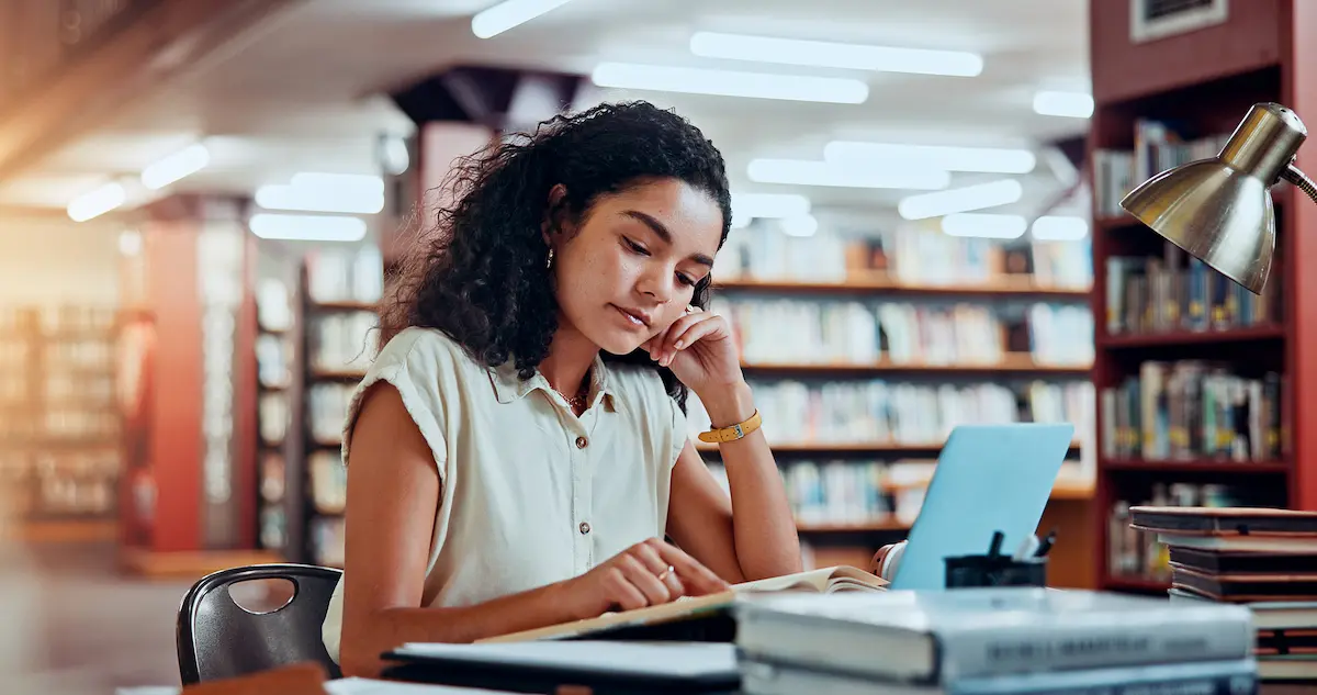 Estudante em biblioteca pesquisa opções de pós-graduação lato sensu e stricto sensu.