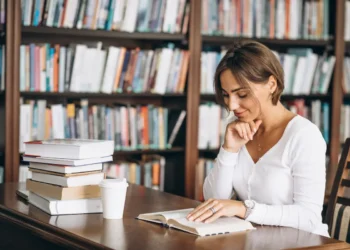 Estudante pesquisa em biblioteca para escolher entre pós-graduação lato sensu e stricto sensu.