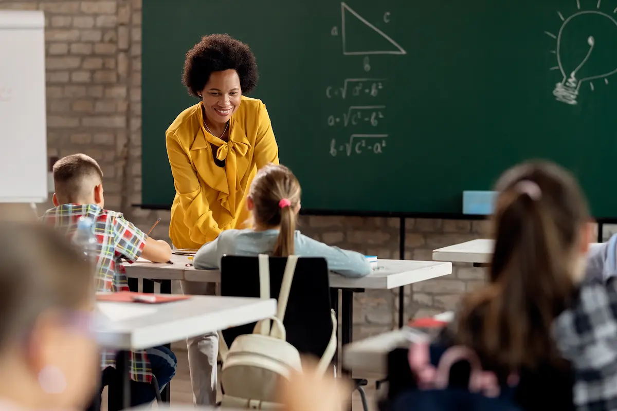 Professora em sala de aula orientando estudantes durante atividade escolar.