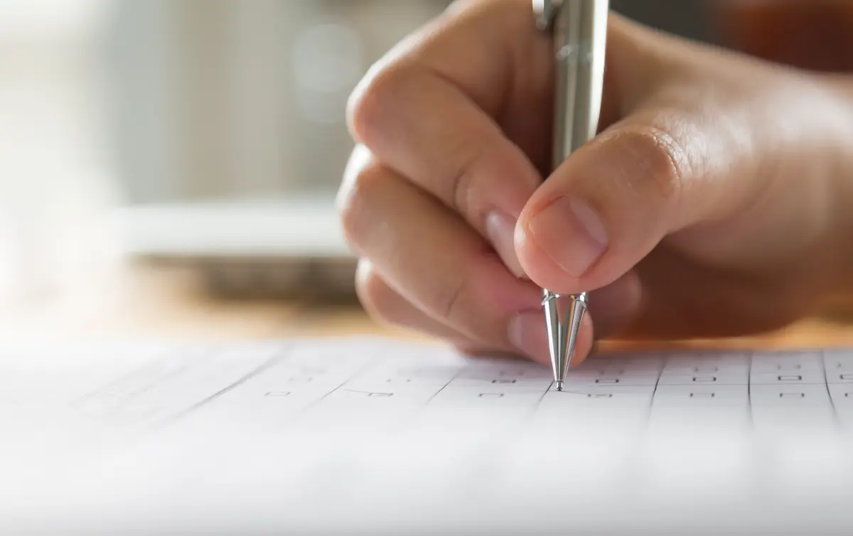 Mão preenchendo prova escrita representando a preparação de estudos para o concurso PC BA Investigador.