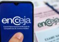 Imagem ilustrativa de celular exibindo a marca do Encceja em frente a cartões de resposta e lápis sobre a mesa, em referência aos preparativos na véspera do exame