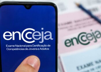 Imagem ilustrativa de celular exibindo a marca do Encceja em frente a cartões de resposta e lápis sobre a mesa, em referência aos preparativos na véspera do exame
