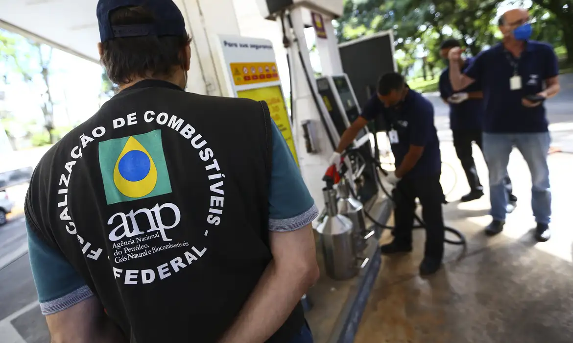 Servidor com colete de fiscalização de combustíveis acompanha coleta de amostra em um posto, em imagem ligada à atuação da agência reguladora.
