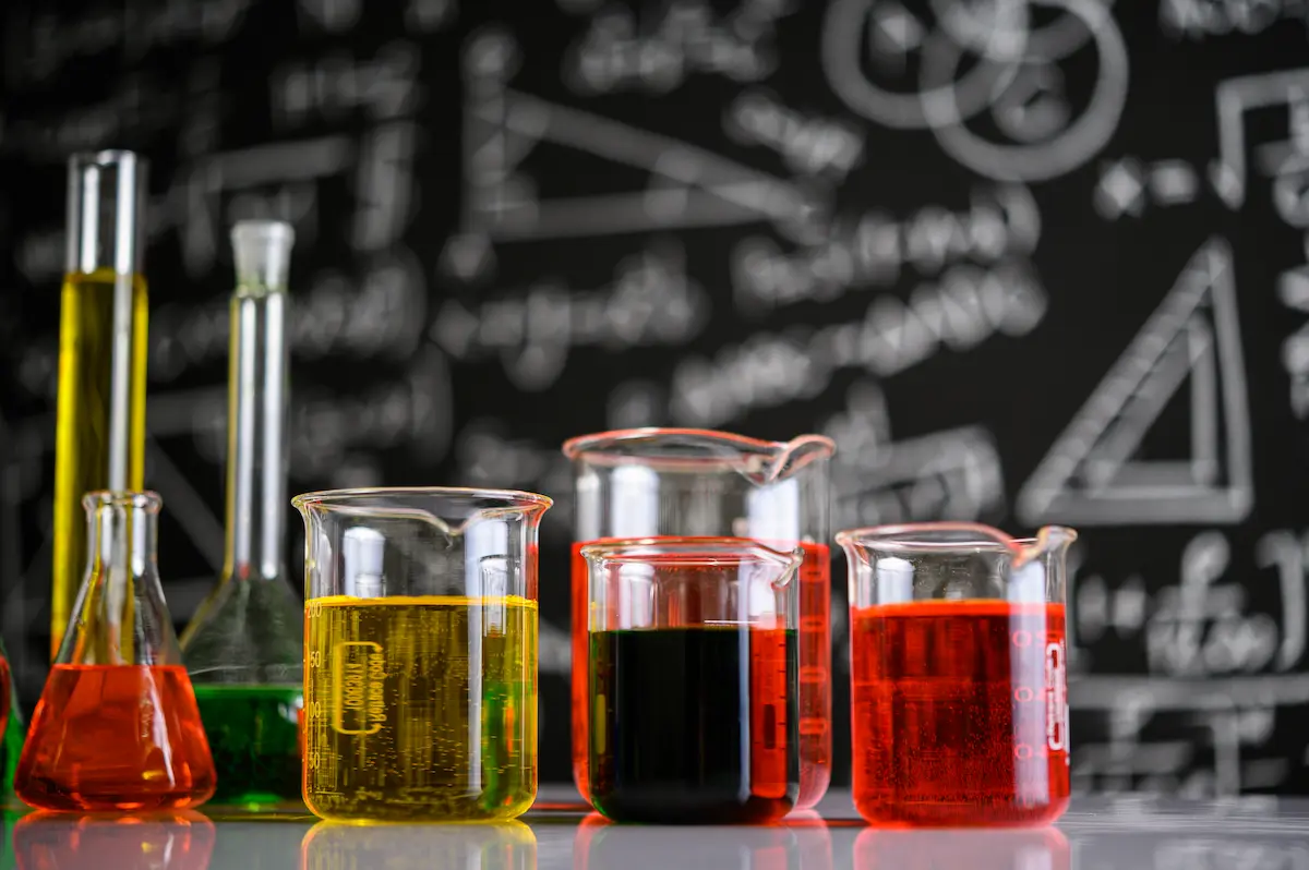 Vidrarias de laboratório com líquidos coloridos representando os temas de Química mais cobrados no Enem.