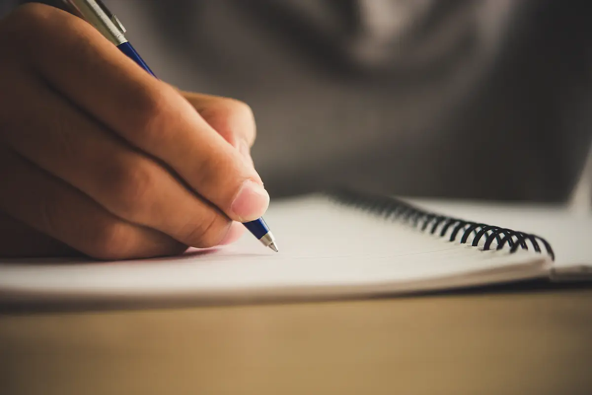 Mão de estudante escrevendo em caderno durante preparação para a redação do Encceja 2026.