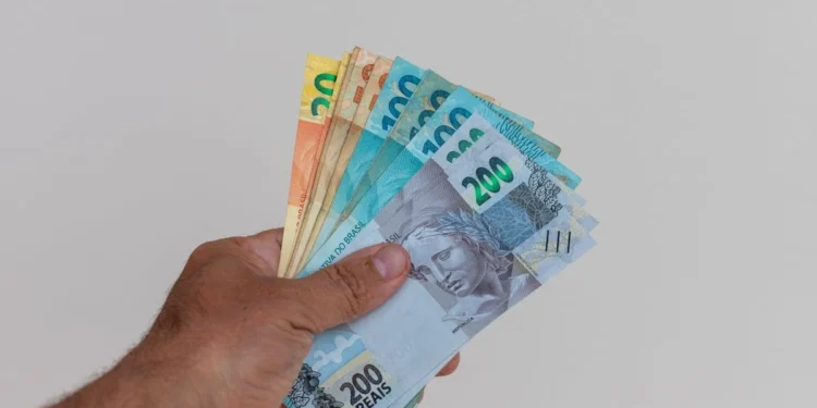 Mão segurando cédulas de real representa a liberação do saque-aniversário do FGTS para trabalhadores nascidos em setembro.