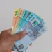 Mão segurando cédulas de real representa a liberação do saque-aniversário do FGTS para trabalhadores nascidos em setembro.