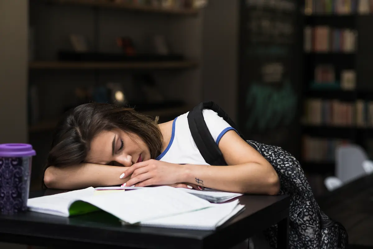Estudante dorme sobre livros após período de estudos, representando falta de sono adequado e cansaço.