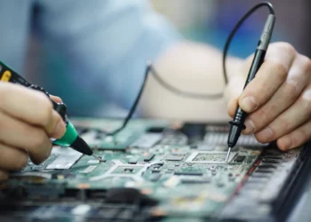 Técnico realizando manutenção em placa de notebook durante reparo de componentes eletrônicos.