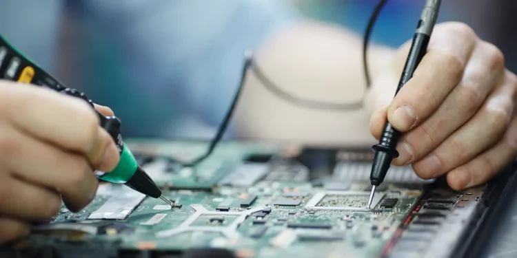 Técnico realizando manutenção em placa de notebook durante reparo de componentes eletrônicos.
