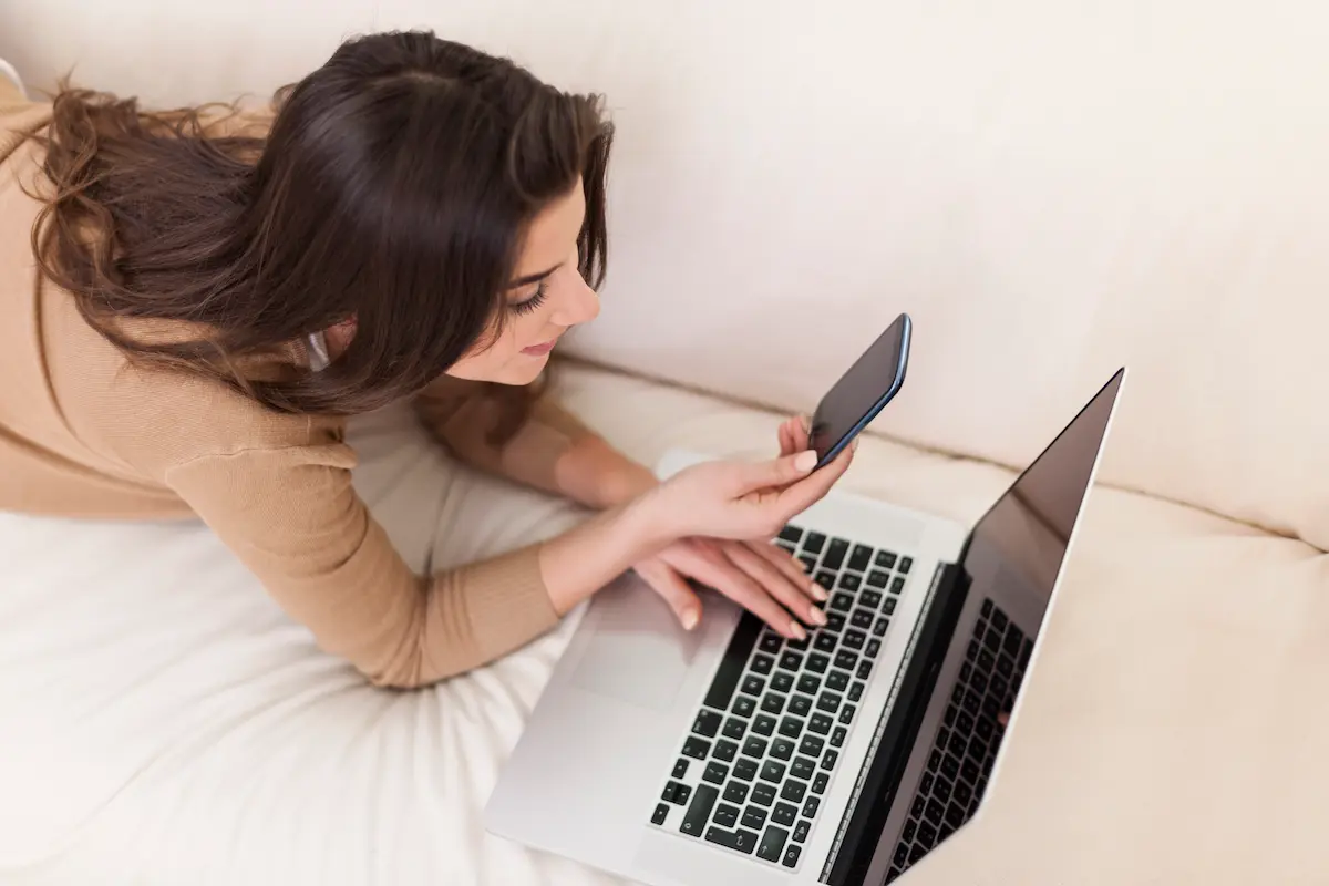 Mulher acessa notebook e celular para consultar oportunidades de emprego e realizar candidatura no Sicoob.