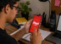 Estudante acessa o aplicativo do iFood pelo celular durante rotina de estudos.