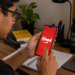 Estudante acessa o aplicativo do iFood pelo celular durante rotina de estudos.