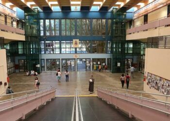 Saguão de acesso a um prédio universitário com estudantes circulando, em imagem ligada à abertura das inscrições do vestibular.