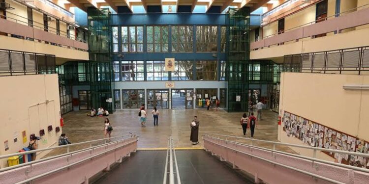 Saguão de acesso a um prédio universitário com estudantes circulando, em imagem ligada à abertura das inscrições do vestibular.