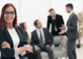 Mulher confiante em ambiente corporativo moderno e equipe no fundo.