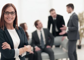 Mulher confiante em ambiente corporativo moderno e equipe no fundo.