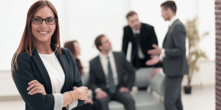Mulher confiante em ambiente corporativo moderno e equipe no fundo.