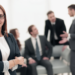 Mulher confiante em ambiente corporativo moderno e equipe no fundo.