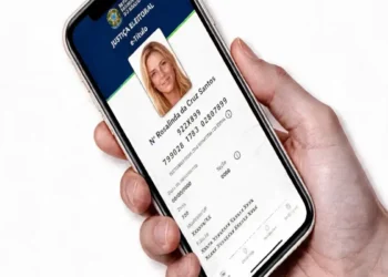 Pessoa segurando celular exibindo tela de e-Título da Justiça Eleitoral com foto de mulher, simbolizando o prazo para acesso do app para a eleição de 2026.
